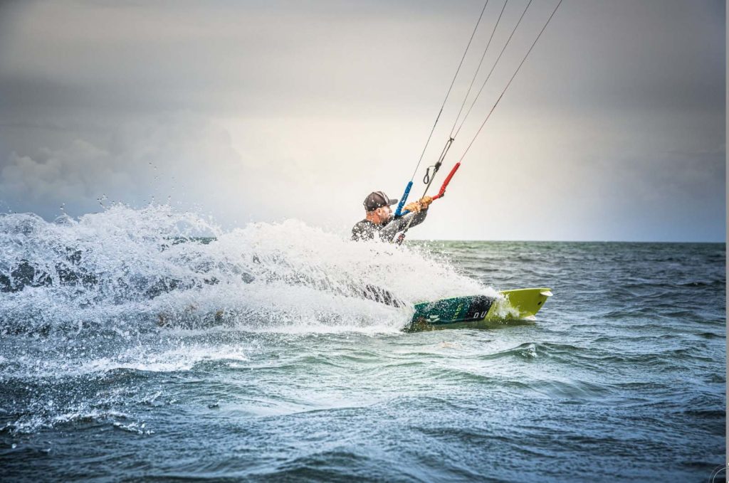 homme expert glisse en kitesurf guadeloupe avec belle gerbe d'eau